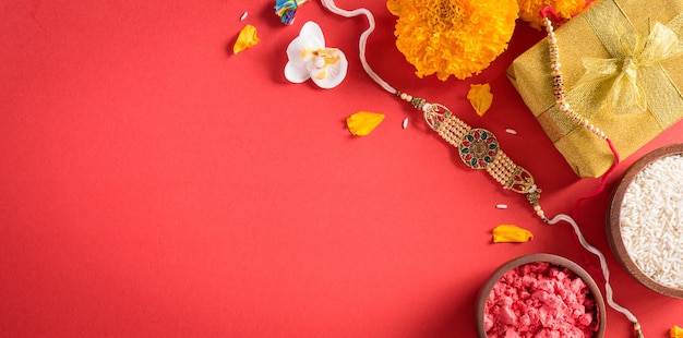 Raksha Bandhan Indian festival with beautiful Rakhi and  Rice Grains on red background