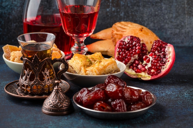 Ramadan kareem Iftar evening meal with dates, baklava, traditional Arabic sweets, fruit, Arab tea, rose sherbet beverage in glass jug. Islamic festive decorated dinner, Ramadan food composition