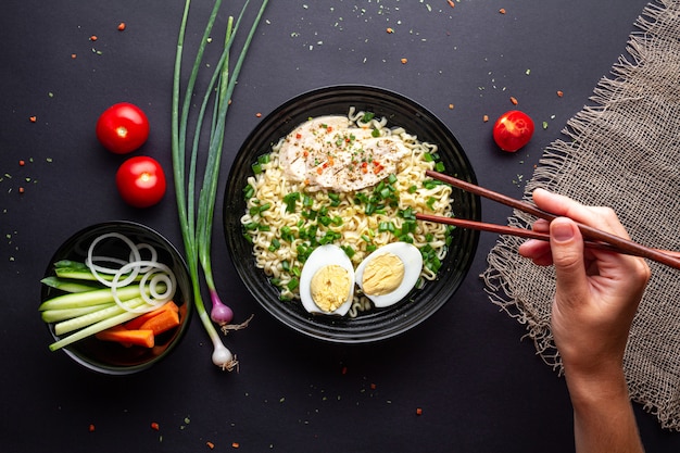 Ramen noodles bowl with chicken, vegetables and egg on black background Top view.