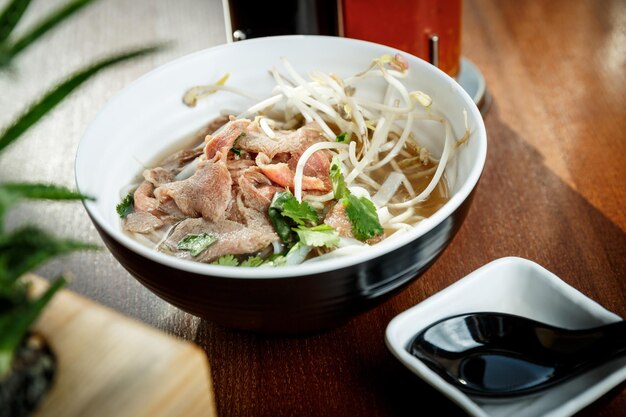 子牛肉のラーメンスープとアジア料理レストランの木製テーブルのボウルに大豆もやしを発芽させた