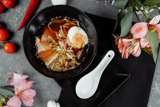 Ramen with chicken, tofu, vegetables and egg in black bowl