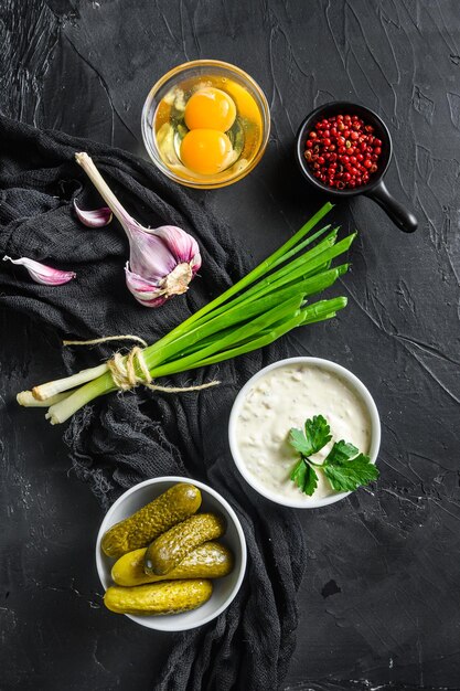 Ranch sauce in a white porcelain bowl with vegetables, herbs and spices on old textured black stone table top view vertical.