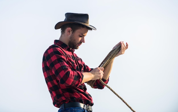 Ranch worker Eco farm Life at ranch Cowboy with lasso rope sky background Farming concept Handsome man in hat and rustic style outfit Keep ranch Thoughtful farmer thinking about business