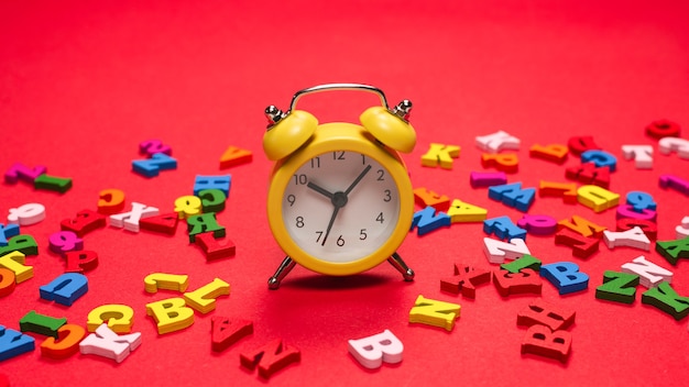 Random colorful alphabet and yellow alarm clock on a red background, colorful letters. Time to school. Study time. Education time.