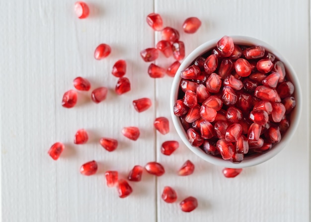 Randomly scattered seeds of ripe pomegranate on a white wooden table. Vegetarian food. Raw food