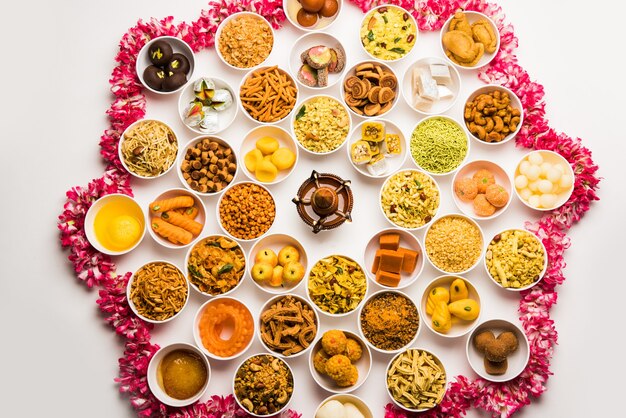 Rangoli of sweets and Farsan or snacks in bowls for Diwali with diya over white background