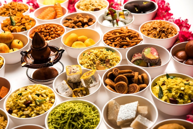 Rangoli of sweets and Farsan or snacks in bowls for Diwali with diya over white background