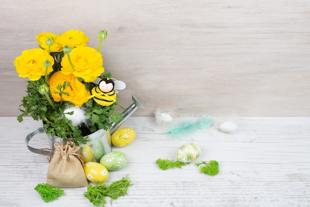 ranunculus buttercups in a metal watering can, decorative bee, Easter painted eggs with feathers, a canvas bag.