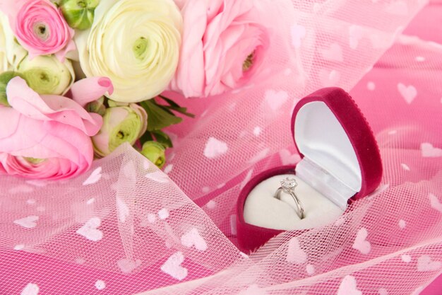 Ranunculus (persian buttercups) and engagement ring, on pink cloth