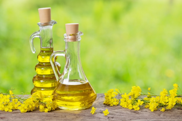 Rapeseed oil (canola) and rape flowers on wooden table