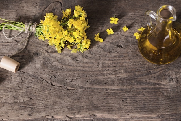 Rapeseed oil (canola) and rape flowers on wooden table