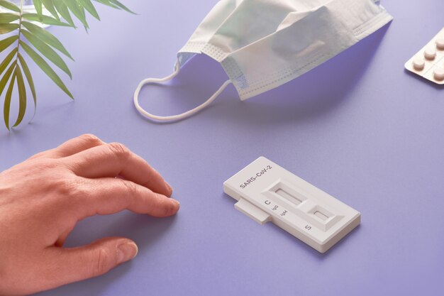 Rapid COVID-19 test for detection of specific antibodies IgM and IgG to novel corona virus SARS-CoV-2 causing Covid-19 disease. Senior hand and test on purple background with plant and glasses.