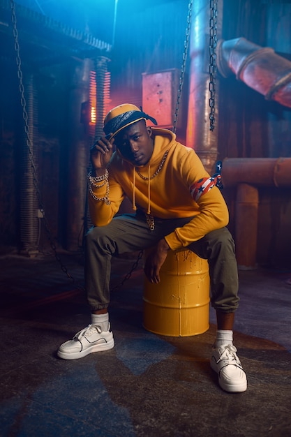 Rapper in yellow hoodie poses in studio with cool underground decoration. Hip-hop performer, rap singer, break-dance