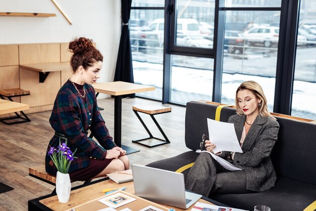 Rapport geven. Krullende persoonlijke secretaresse met een mooie ketting en een stijlvol kostuum die verslag uitbrengt aan haar baas