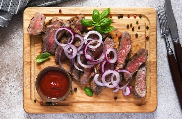 Rare beef steak with onion, slice on a wooden board. View from above.