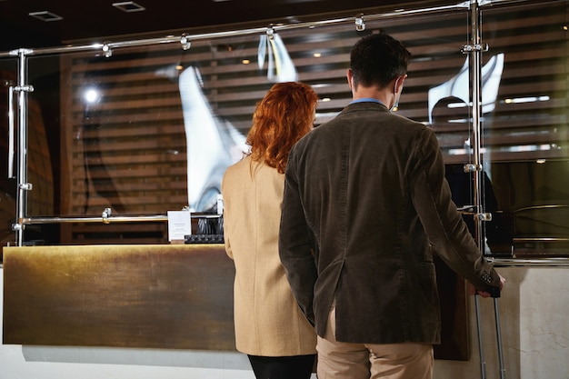 Rara veduta di una coppia adulta in piedi davanti a uno scudo di vetro sul piano di lavoro durante il check-in. modello banner