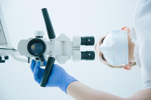 Rare view photo of a modern dental microscope and a female medical worker in mask and rubber gloves using it