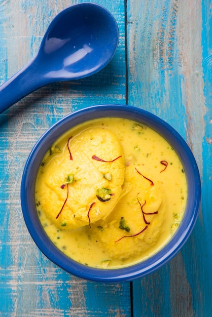 Ras malai 또는 rossomalai는 인도 벵골의 디저트입니다. 사프란이나 케사르&피스타치오 토핑을 얹은 크러스트가 없는 진한 치즈케이크입니다. 나무 또는 화려한 배경 위에 그릇에 제공