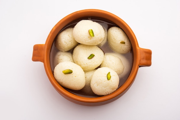 Foto rasgulla of rosogulla - een indiaas snoepje gemaakt van khoya, zacht en sponsachtig, in aarden kom over gele servet en bruine achtergrond