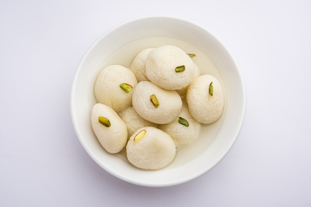 Расгулла или розогулла - индийская сладость из койи, мягкая и пористая, в глиняной посуде на желтой салфетке и коричневом фоне.