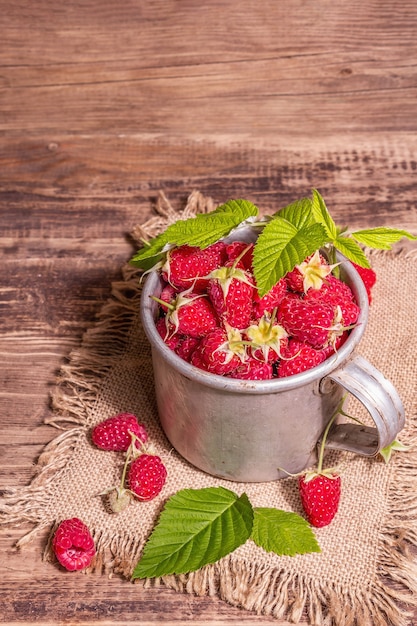 Raspberries background. Ripe fruits in a vintage mug, rustic style. Modern hard light, dark shadow. Old wooden boards table, copy space