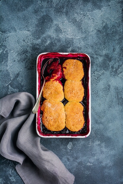 Raspberries and black currants cobbler with raspberry ice cream in baking dish. Homemade fruit pie pastries. Gray vintage background. Top view.