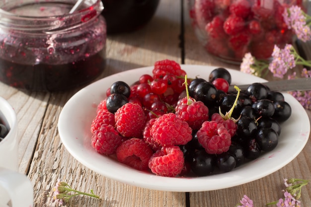 Raspberries, black and red currant on the plate and jam