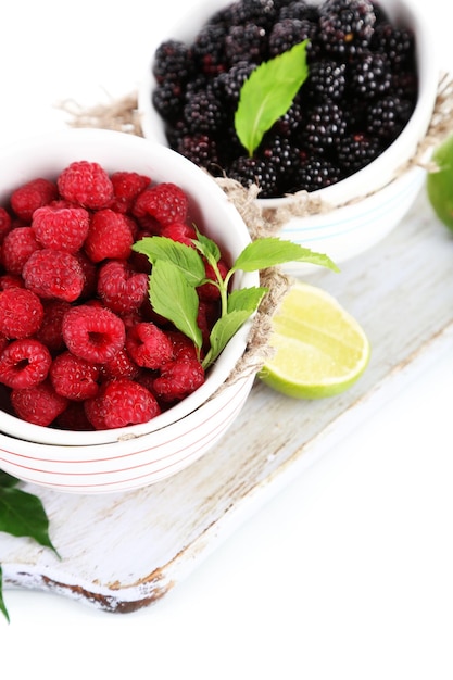 Raspberries and blackberry in small bowls on board isolated on white