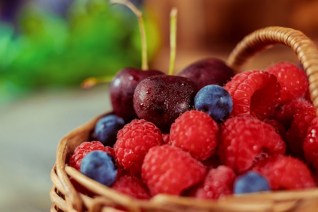 Raspberries and blueberries in a basket with handle and couple cherries