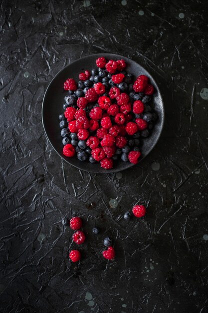 Raspberries and blueberries, on a black background, wild berry