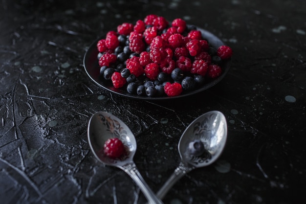 Photo raspberries and blueberries, on a black background, wild berry