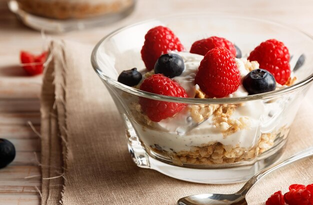 Photo raspberries blueberries cereals and yogurt in a glass bowl on sackcloth and wooden slats healthy