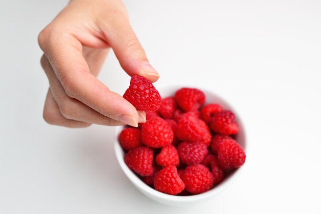 Raspberries in a bowl in hand on a white background isolation Female hand holding a raspberry Red raspberry in hand Healthy eating dieting vegetarian food and people concept