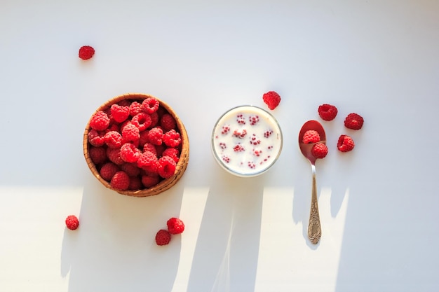 Raspberries in bowl with cup of milk on white background. Top view