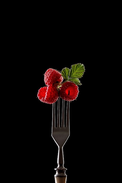 Raspberries on fork against black background. Healthy eating concept