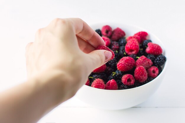 Raspberries in hand on a white background in a plate with berries