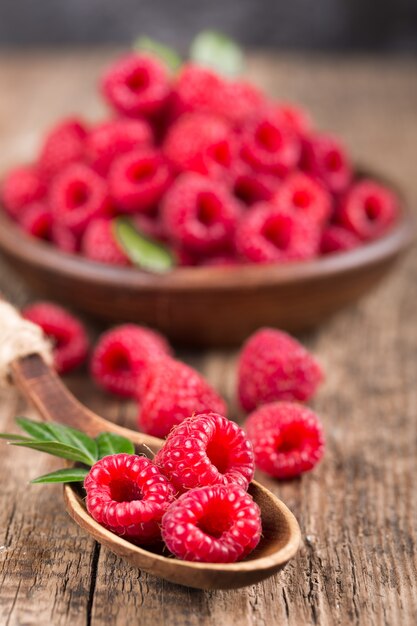 Raspberries in plate and spoon on wooden table