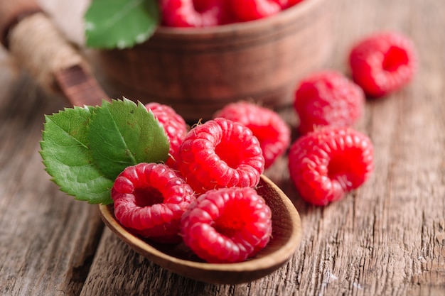 Raspberries in spoon on wooden table.