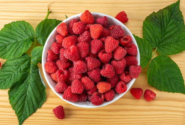 Raspberries on white plate on wooden table with leaves Organic raspberries grown without use of chemical fertilizers and pesticides Raspberries on wooden background top view