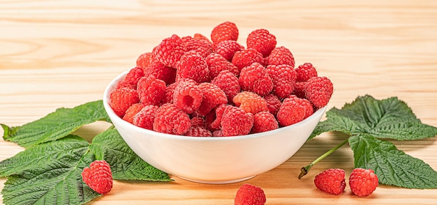 Raspberries on white plate on wooden table with leaves Organic raspberries grown without use of chemical fertilizers and pesticides Raspberries on wooden background