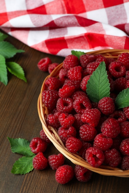 Raspberries in a wicker bowl and a tea towel on a wooden table.