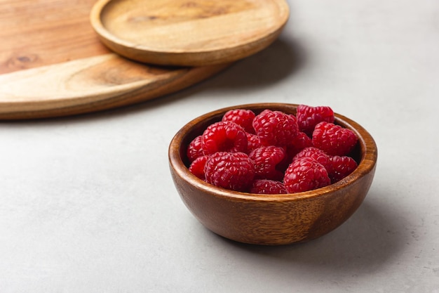 Raspberries in a wooden bowl on a light grey background Fresh red berries