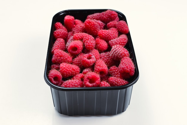 Raspberry in black container isolated on white background.