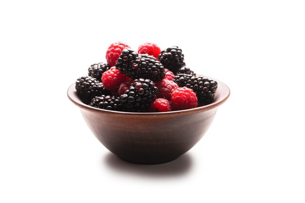 Raspberry, blackberry and mint leaf in ceramic brown bowl isolated on white surface.