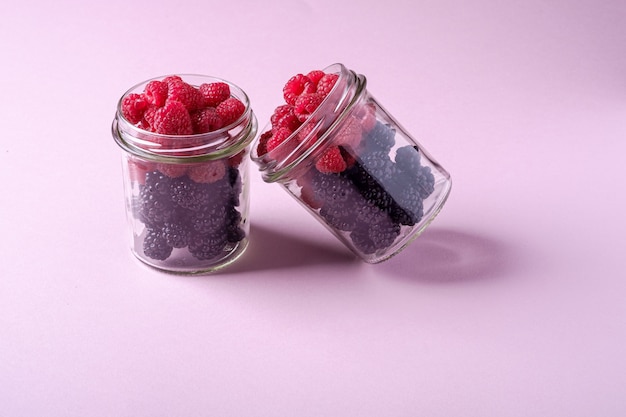 Raspberry and blackberry sweet organic juicy berries in two glass jars on pink paper