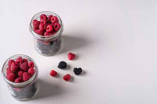 Raspberry and blackberry sweet organic juicy berries in two glass jars on white wooden table