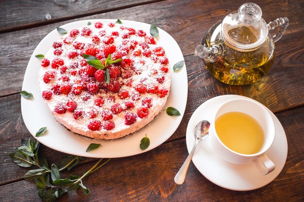 Raspberry cheesecake with green tee on wooden table