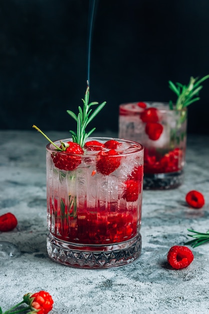 Raspberry coctail in a glass with ice and smoke rosemary on a concrete background. Selective focus