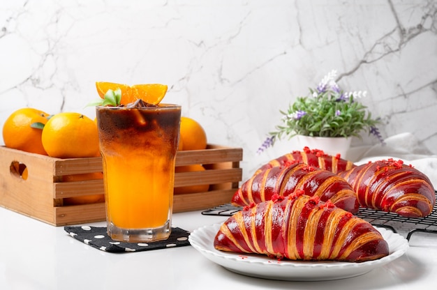 オレンジアメリカーノコーヒーとラズベリークロワッサンは、さわやかな朝に提供する準備ができています。