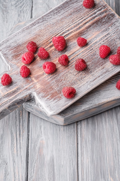 Foto frutti di lampone sul vecchio tagliere, mucchio sano di bacche estive sul bordo di legno grigio, angolo di visione